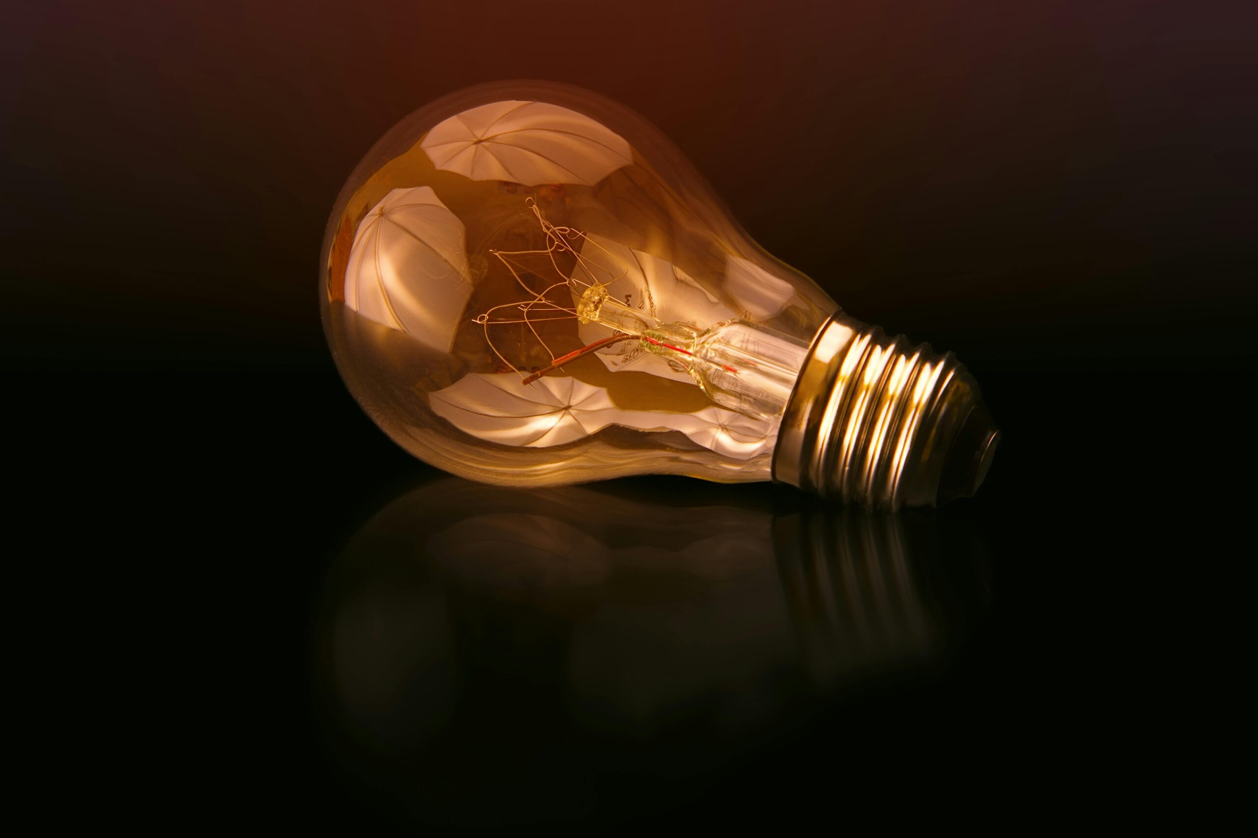 A detailed close-up of a light bulb showcasing its intricate filament and glowing glass against a dark reflective surface.